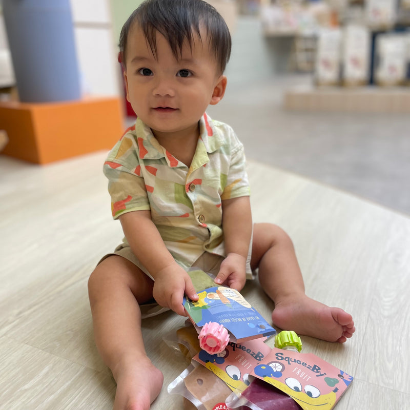 A baby sitting on the floor with Squeezby fruit pouches